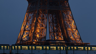 Train passing by foot of illuminated Eiffel Tower at night