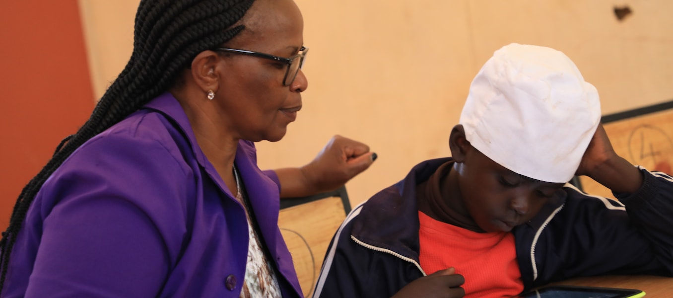 Teacher Jane Njoroge looks on as Frank from Mugumoini Primary School in Thika Town uses his digital tablet. /  ©UNICEFKenya/2019/Ndinda