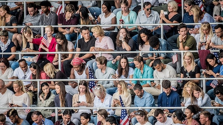 A stadium crowd, many on their phones during a break in action