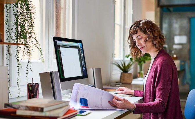 Woman sat at desk in front of computer browsing through print-outs