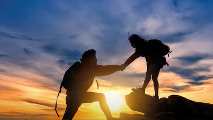Two people helping each other on a mountain climb.
