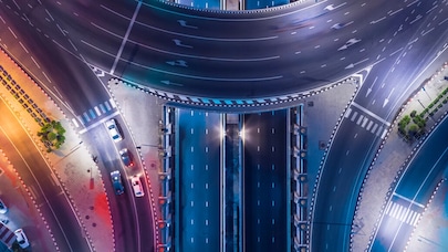 An image of a crossroads at nighttime with bright colourful city lights.