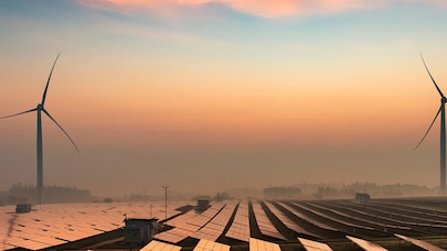 A picture of two wind turbines and many solar panels in a morning haze.