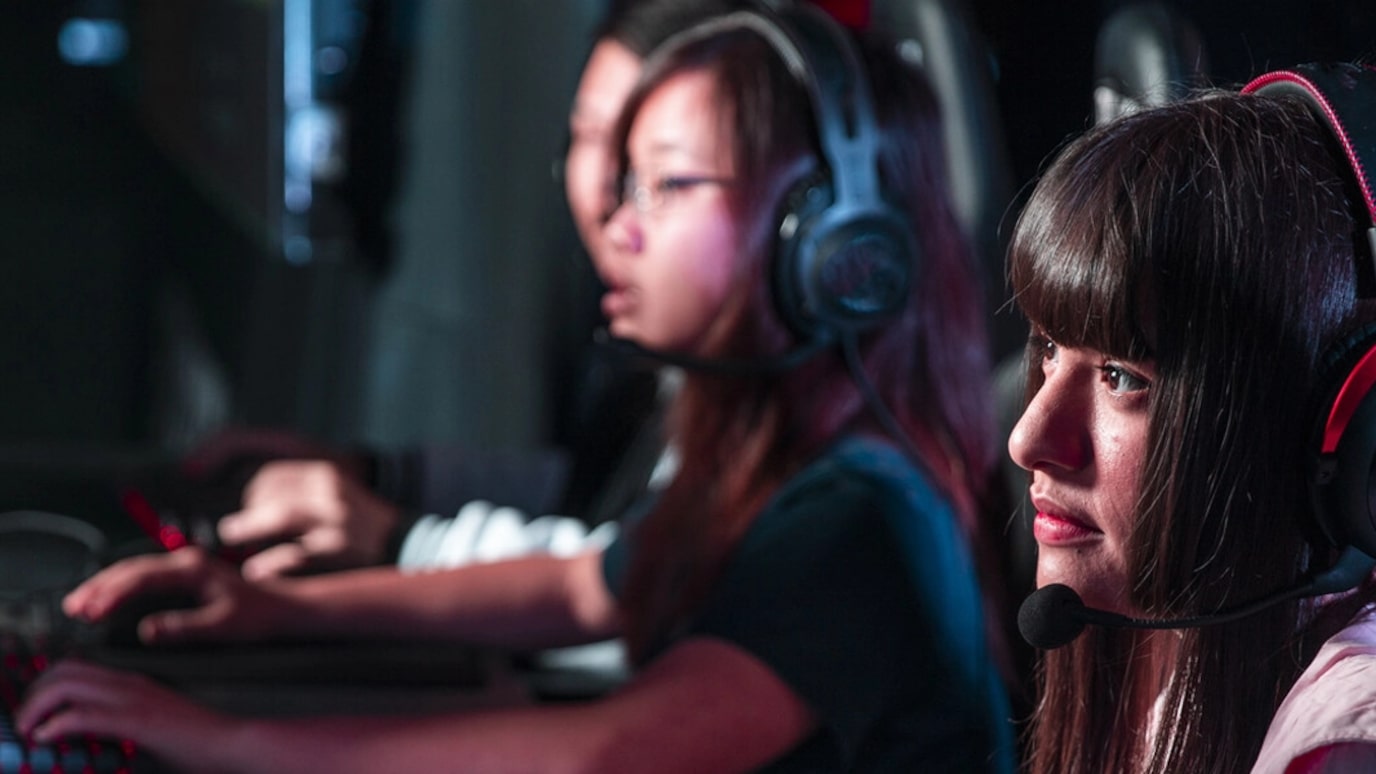 Three young people playing on gaming PCs with headsets on.