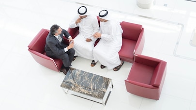An image of three people sitting on red couches discussing something.
