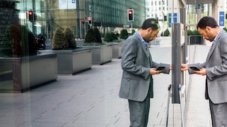 A person standing at an ATM with their reflection showing on a glass wall next to the ATM.