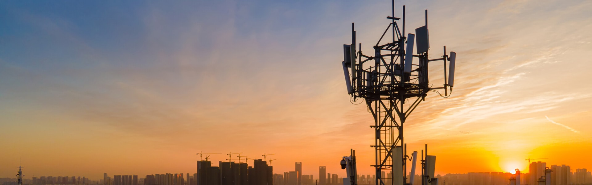 Antenna tower silhouetted against sunset with city skyline in background