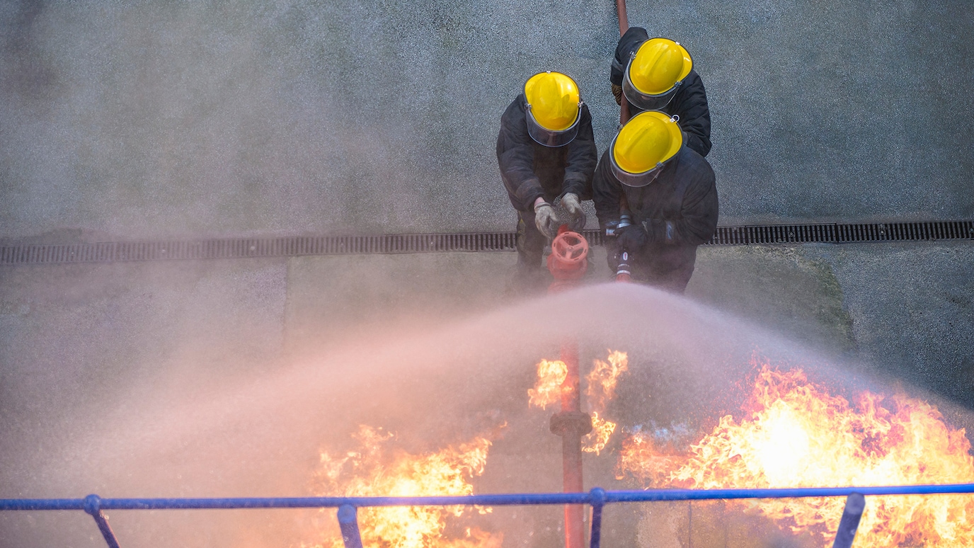 Three firefighters extinguishing fire with hose on wide spray