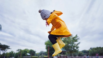 A girl wearing a yellow raincoat jumping in puddle