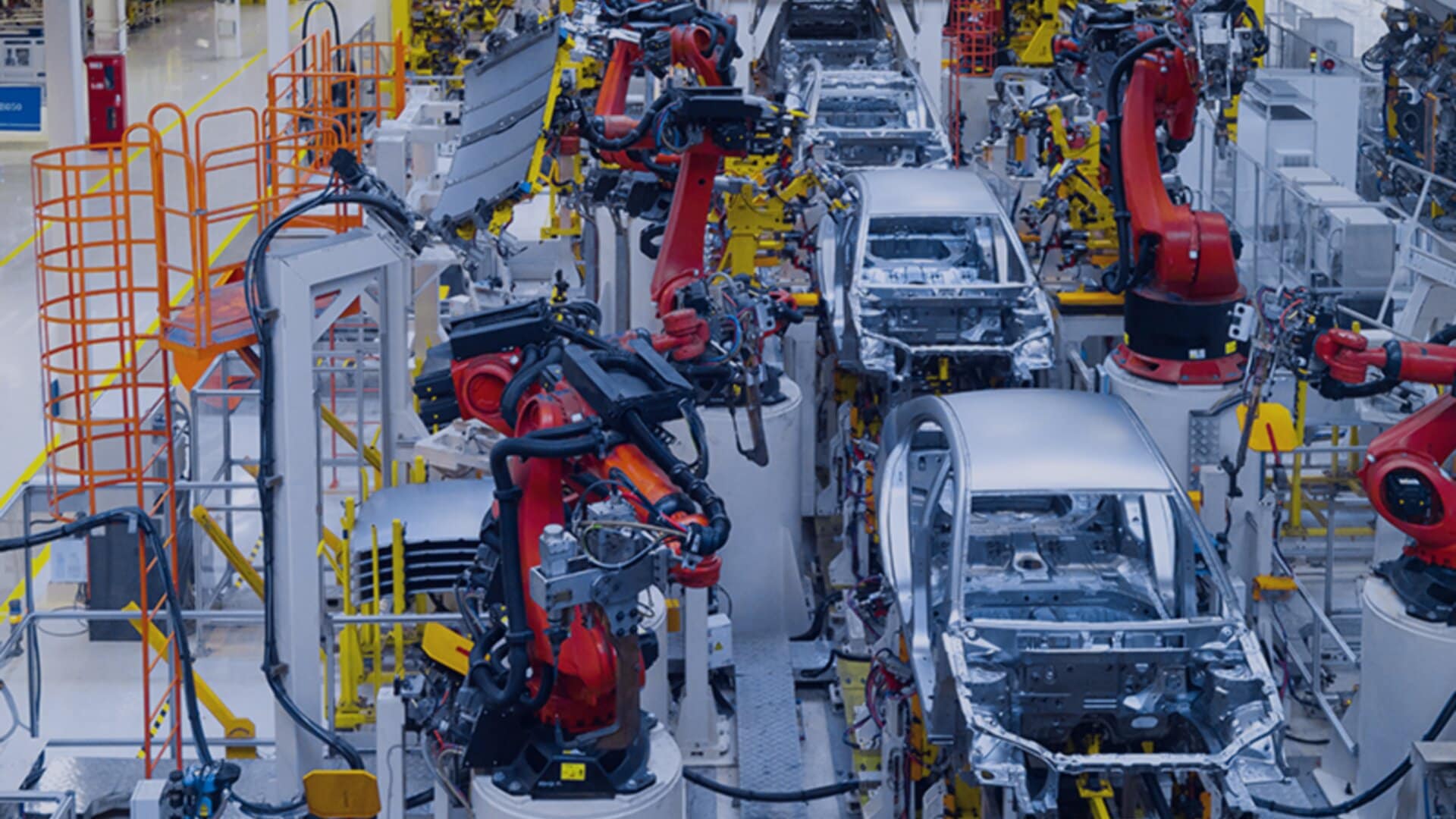 An advanced automotive manufacturing facility. Several robotic arms are actively engaged in assembling car bodies on a production line.