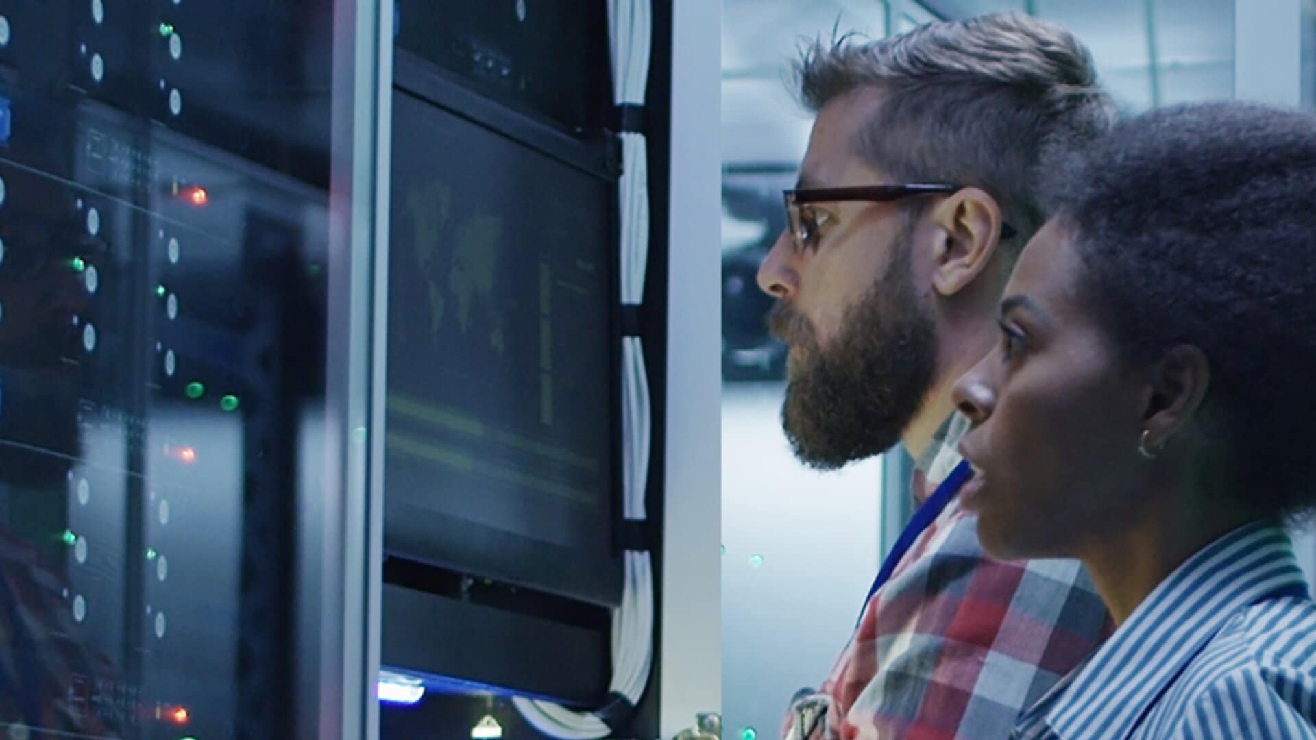 Two IT professionals working in a data center environment. They are standing in front of server racks, examining the equipment closely.