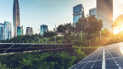 A cityscape with tall buildings and lush greenery. In the foreground, a solar panel array is capturing energy from the sun.