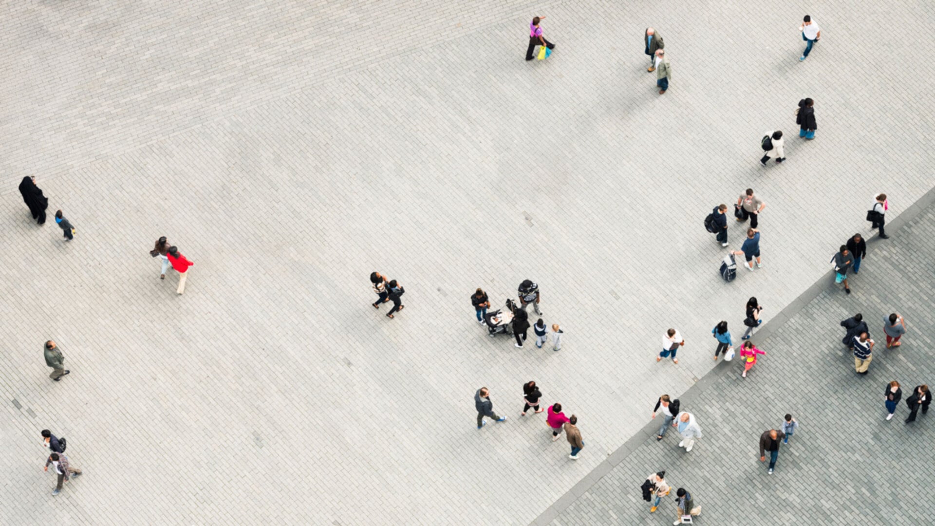 Aerial view of a city plaza with light paving, showing numerous people walking in various directions, creating patterns of urban movement.