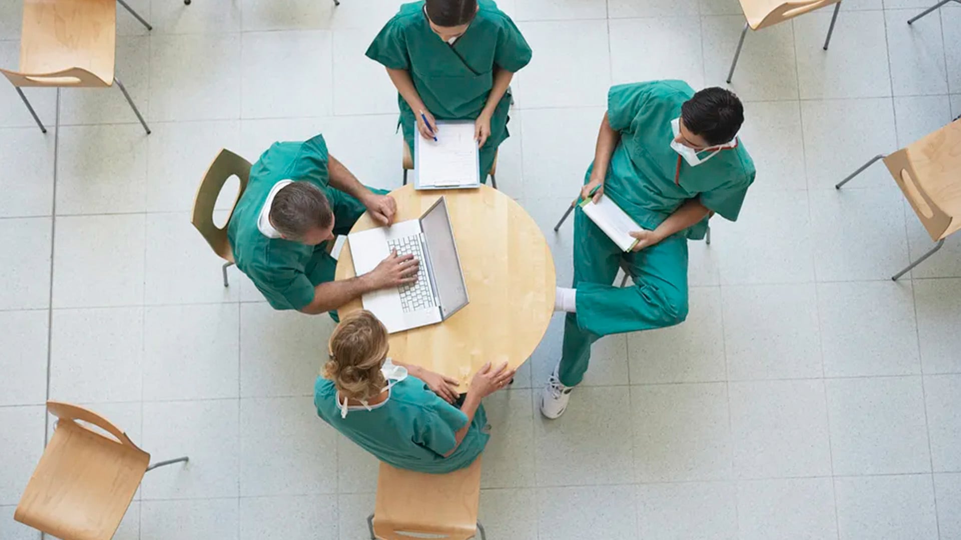 Aerial view of four nurses sat around a table. One is using a laptop.
