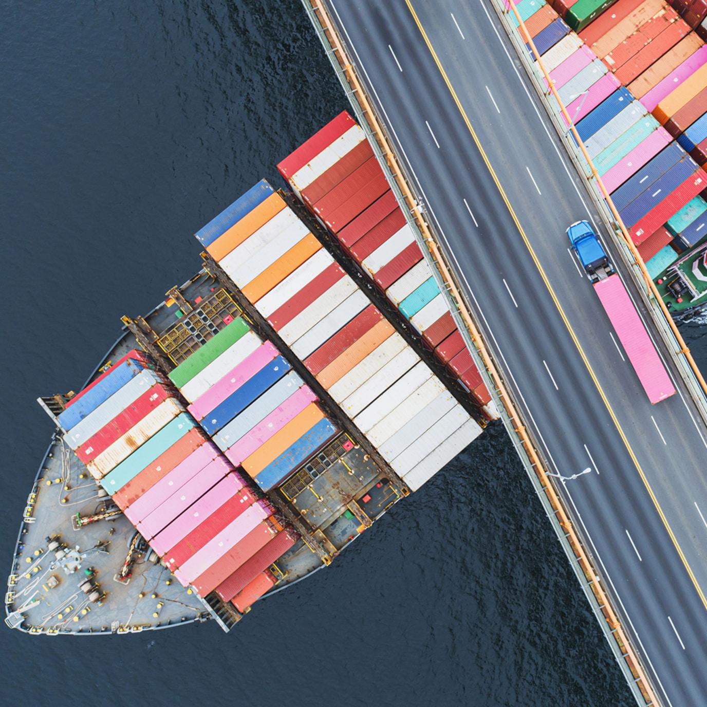 Overhead view of cargo ship with containers on deck passing under bridge
