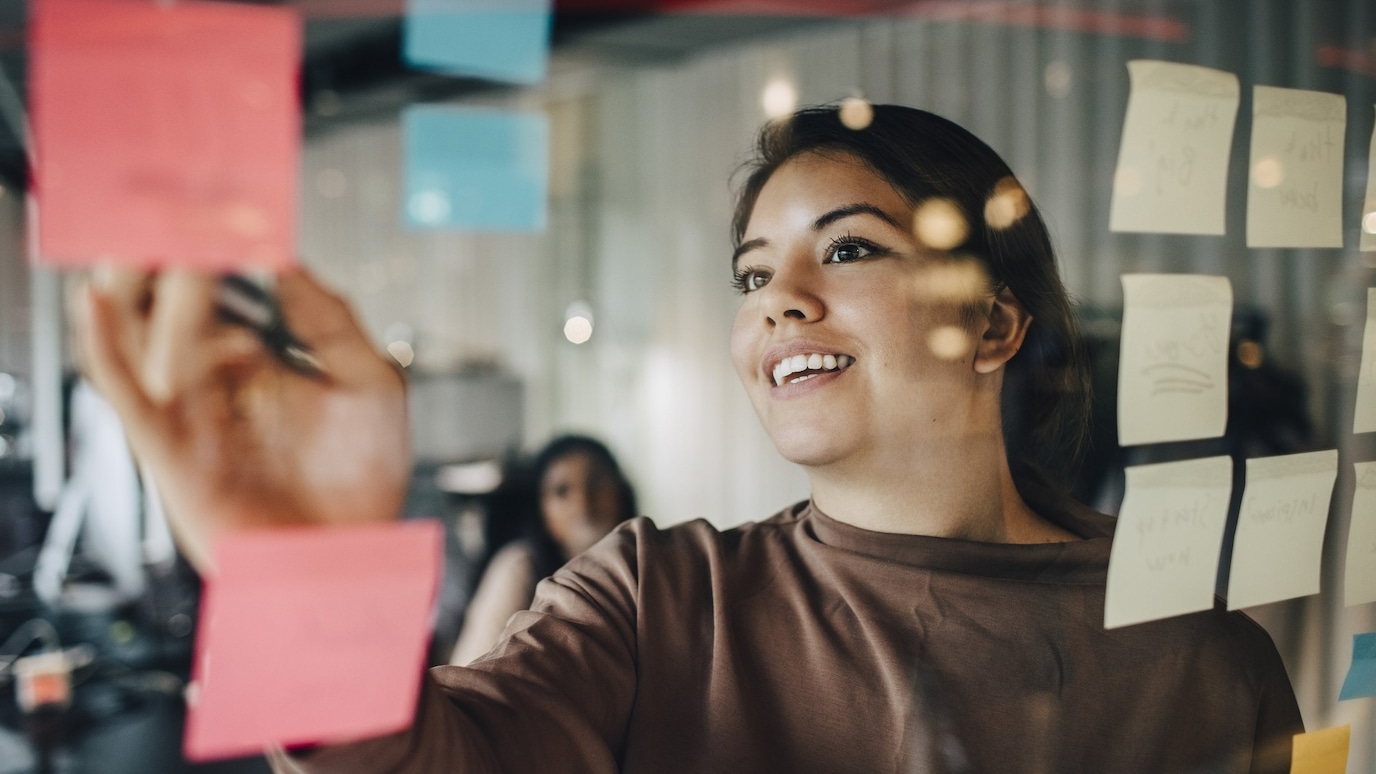 Woman writing on a sticky note pasted on a glass board