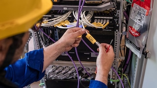 Technician wearing a yellow hard hat and blue uniform labeling cables in a network server rack, ensuring organized cable management.