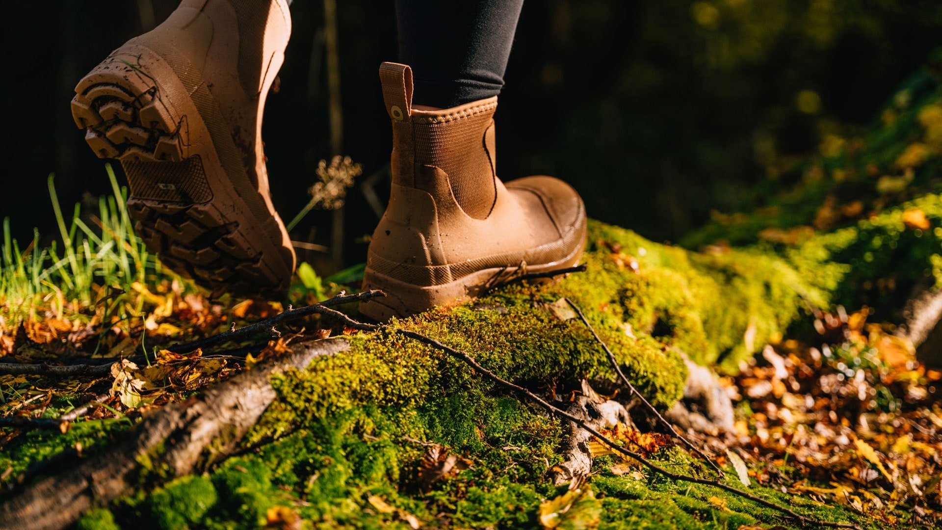 Close-up of a person wearing brown hiking boots stepping on a moss-covered log in a forest during autumn.