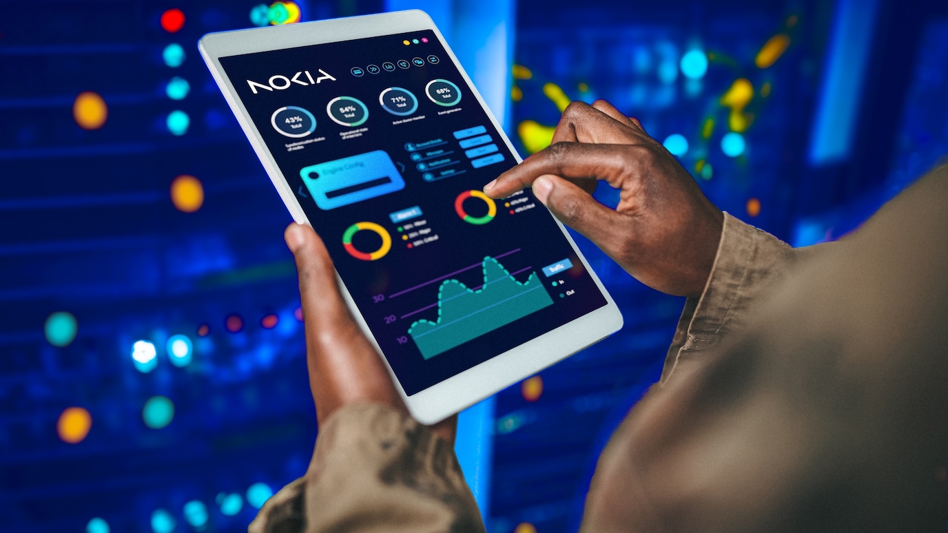 Person analyzing data on a tablet with Nokia dashboard interface, showing charts and metrics in a server room environment.