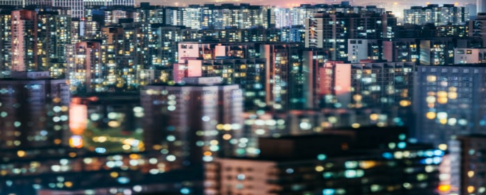 Night cityscape with high-rise apartment buildings lit by thousands of windows, creating a vibrant urban skyline.