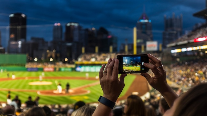 Person filming baseball game in stadium on smartphone