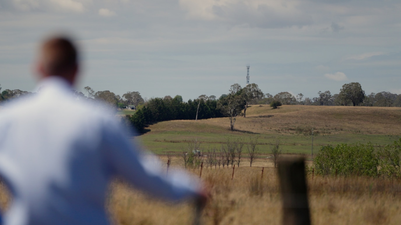 Man looking at radio mast on hill behind fields