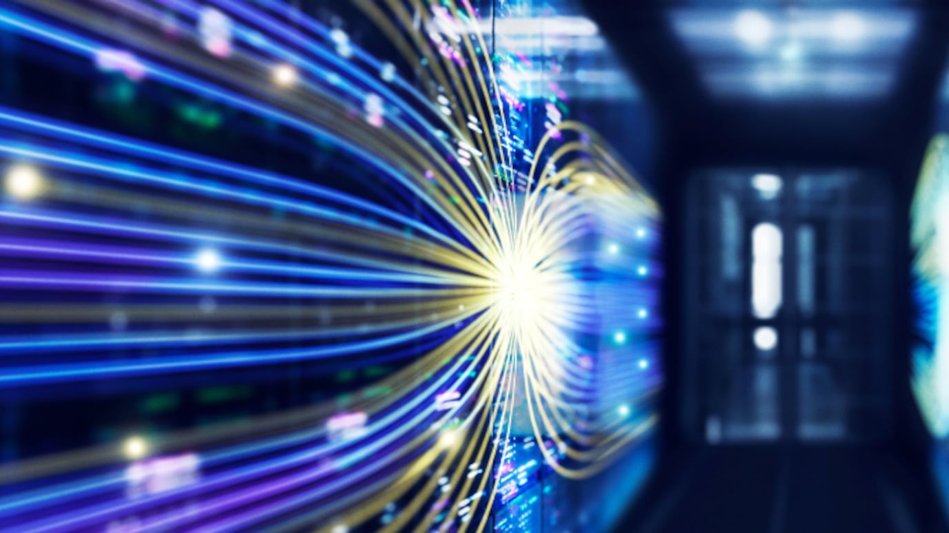 High-speed data transfer visualization showing glowing fiber-optic network cables in a modern data center corridor.