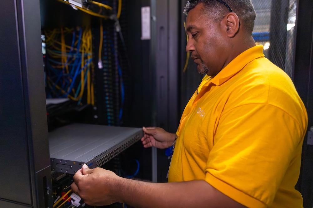 Man standing in a data center, pulling a component from a server rack for maintenance or hardware upgrade.
