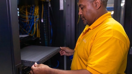 Man standing in a data center, pulling a component from a server rack for maintenance or hardware upgrade.