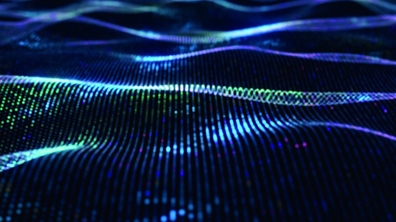 Abstract digital wave of glowing blue and green particles forming futuristic flowing lines on a dark background