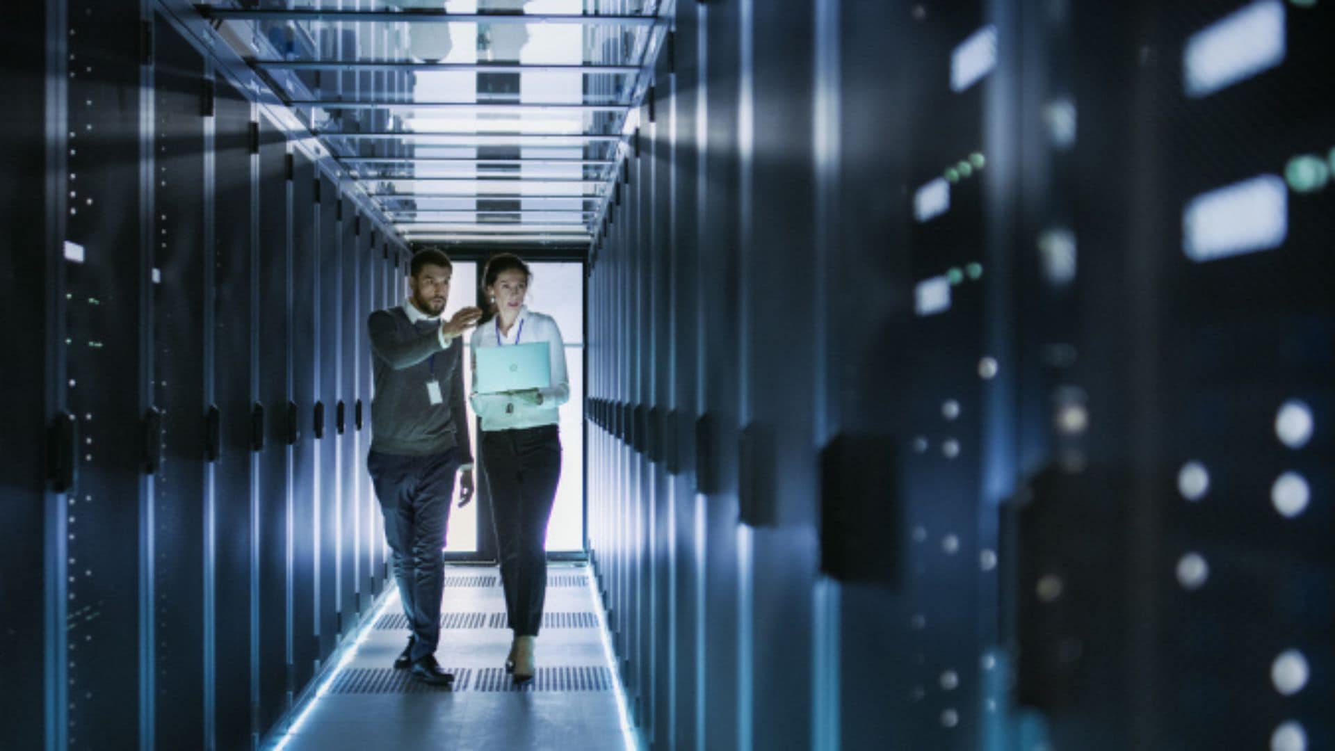 Two workers walking and talking in a modern server room with rows of servers and bright lighting.
