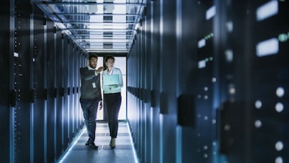 Two workers walking and talking in a modern server room with rows of servers and bright lighting.
