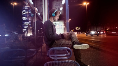 Man sitting at a bus stop wearing headphones and listening to music, enjoying a moment of relaxation in the city.