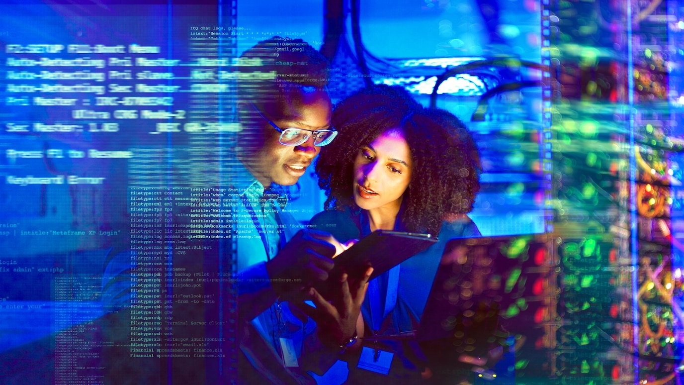 Two IT professionals reviewing data on a tablet in a server room with digital code overlays and network equipment.
