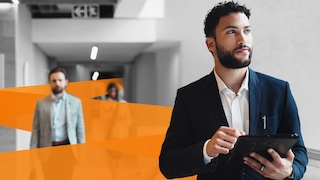 Man standing in office corridor holding tablet device