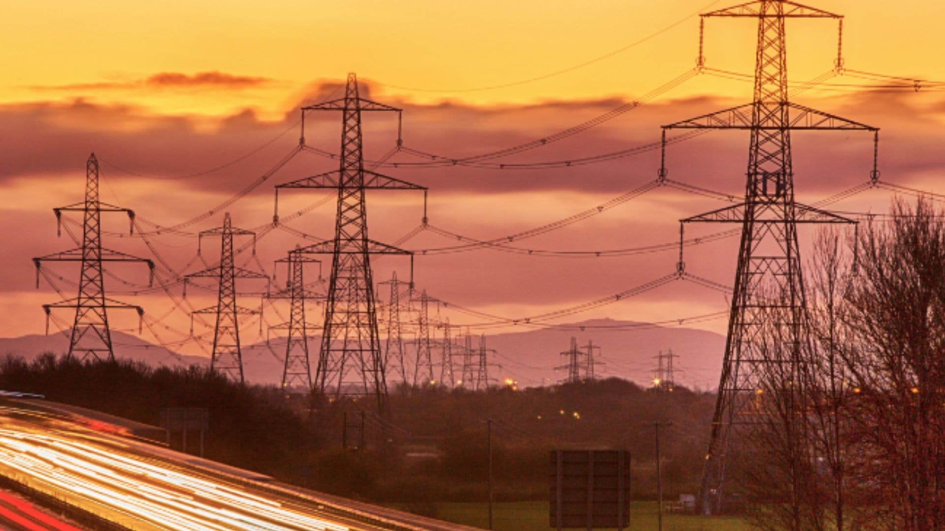 High-voltage power lines and light trails on a highway at sunset, symbolizing energy and connectivity.