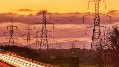 High-voltage power lines and light trails on a highway at sunset, symbolizing energy and connectivity.