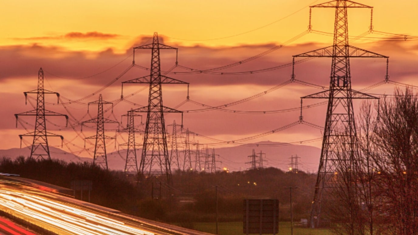 High-voltage power lines and light trails on a highway at sunset, symbolizing energy and connectivity.