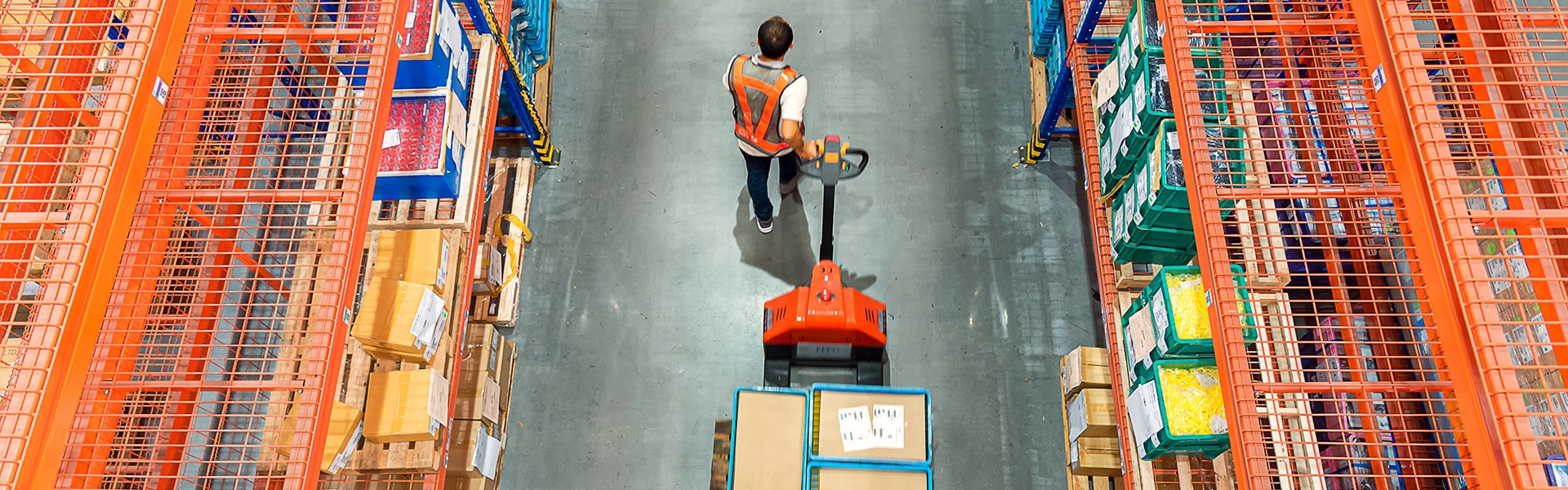 Overhead view of man pulling pallet truck in warehouse, flanked by shelving racks