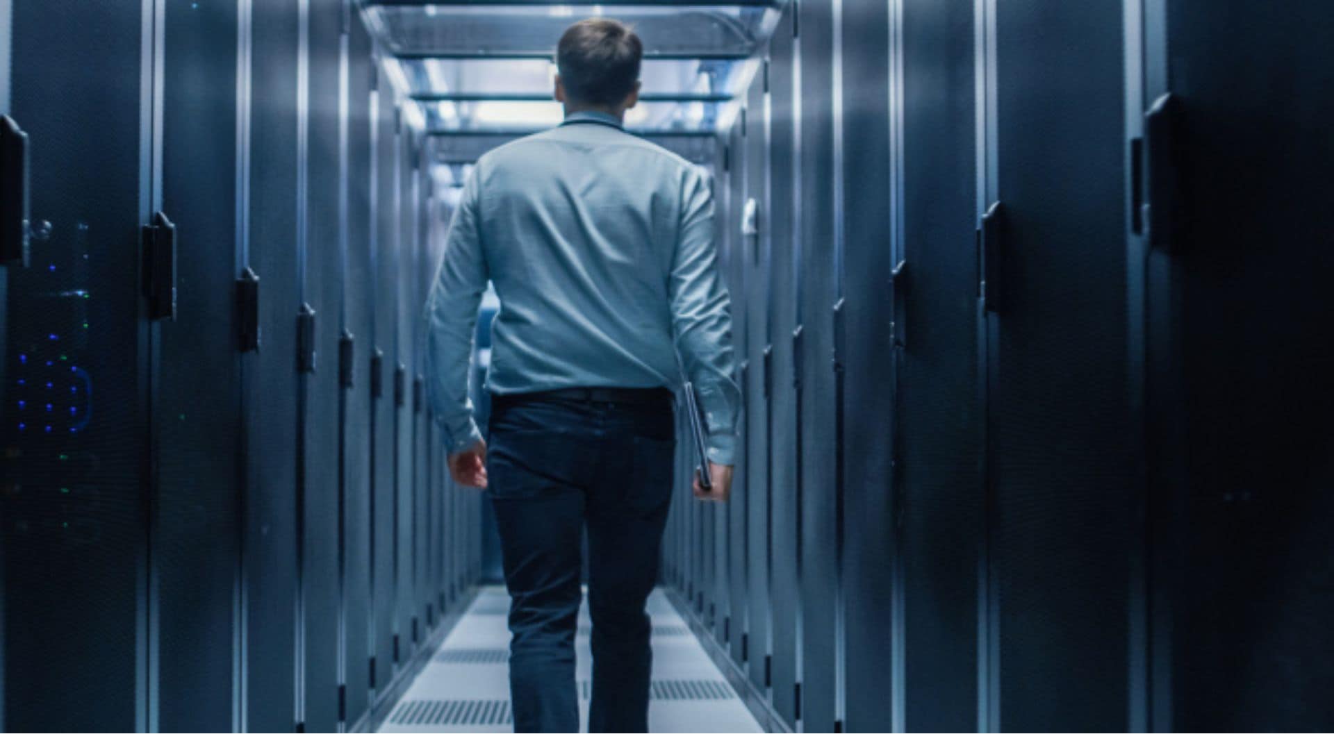 Man walking in a data center with a laptop in his hand.