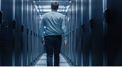 Man walking in a data center with a laptop in his hand.