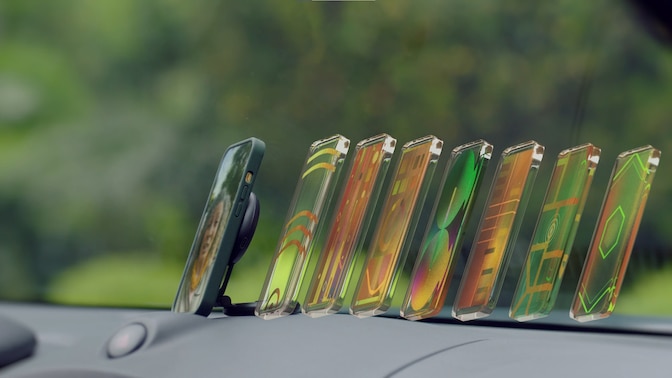 Smartphone in holder on car dashboard with digital representation of multiple screens behind the phone.