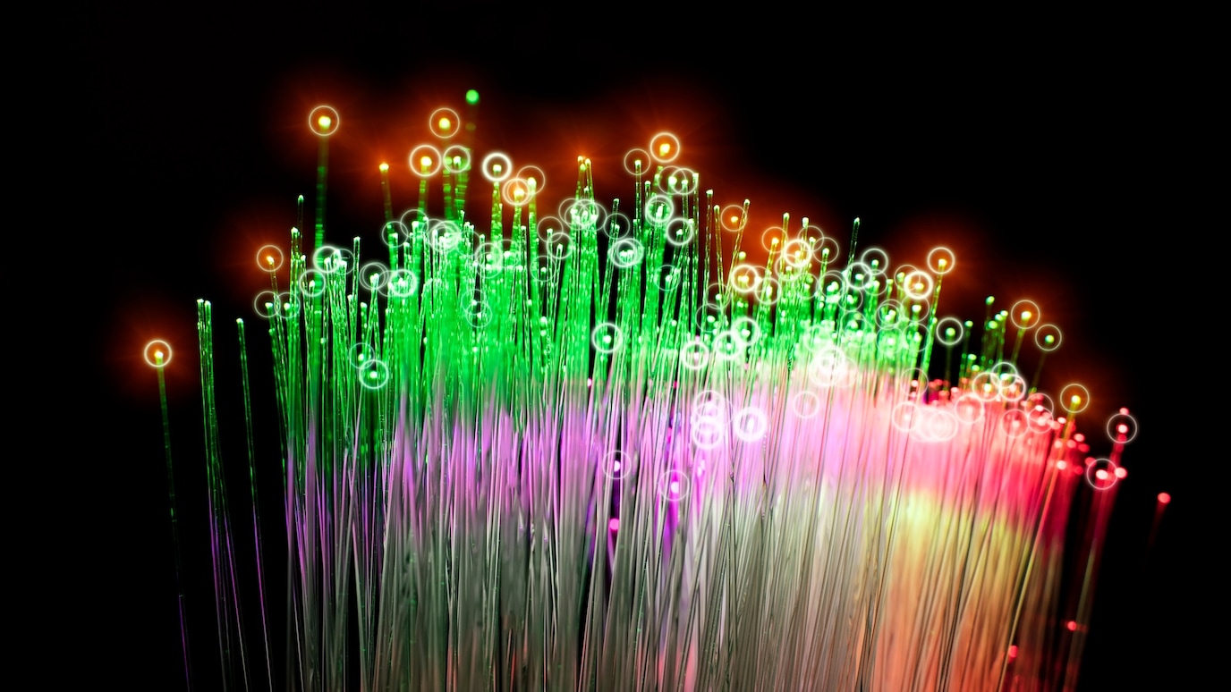 Abstract fiber optic strands glowing green, red and purple on black background, symbolizing data technology