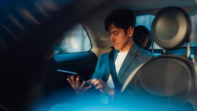 A man sitting in the back seat of a car, looking at a tablet in his hand.