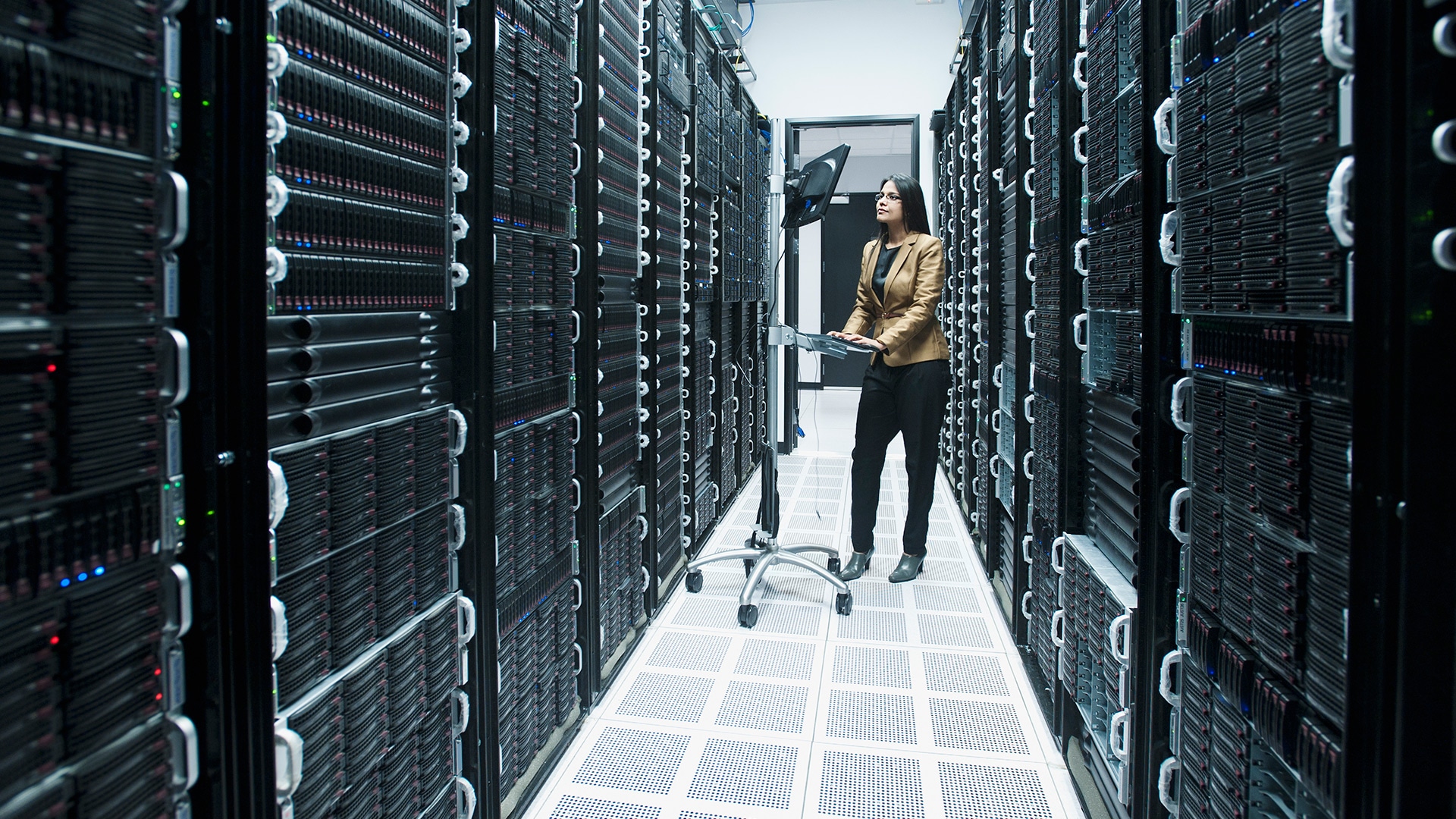 Woman working on wheeled workstation for keyboard and monitor in corridor between racks of servers