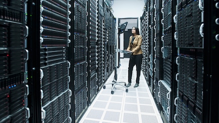 Woman working on wheeled workstation for keyboard and monitor in corridor between racks of servers