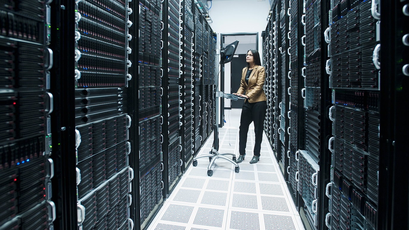Woman working on wheeled workstation for keyboard and monitor in corridor between racks of servers