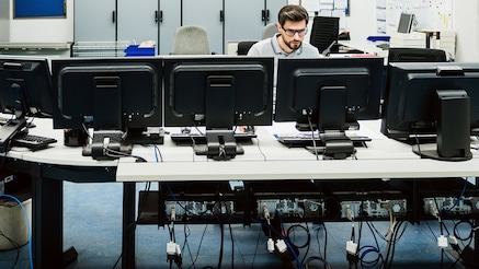 Man sitting at desk facing a bank of monitors