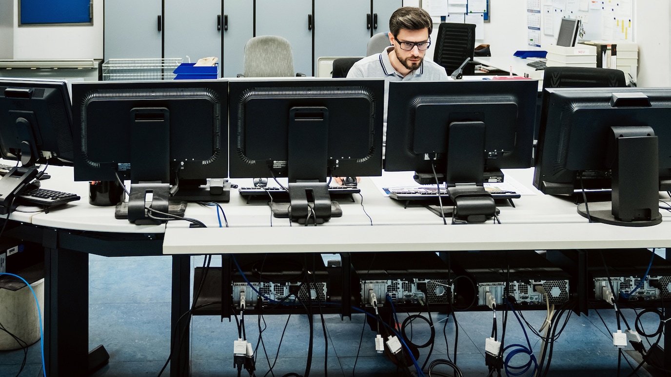 Man sitting at desk facing a bank of monitors