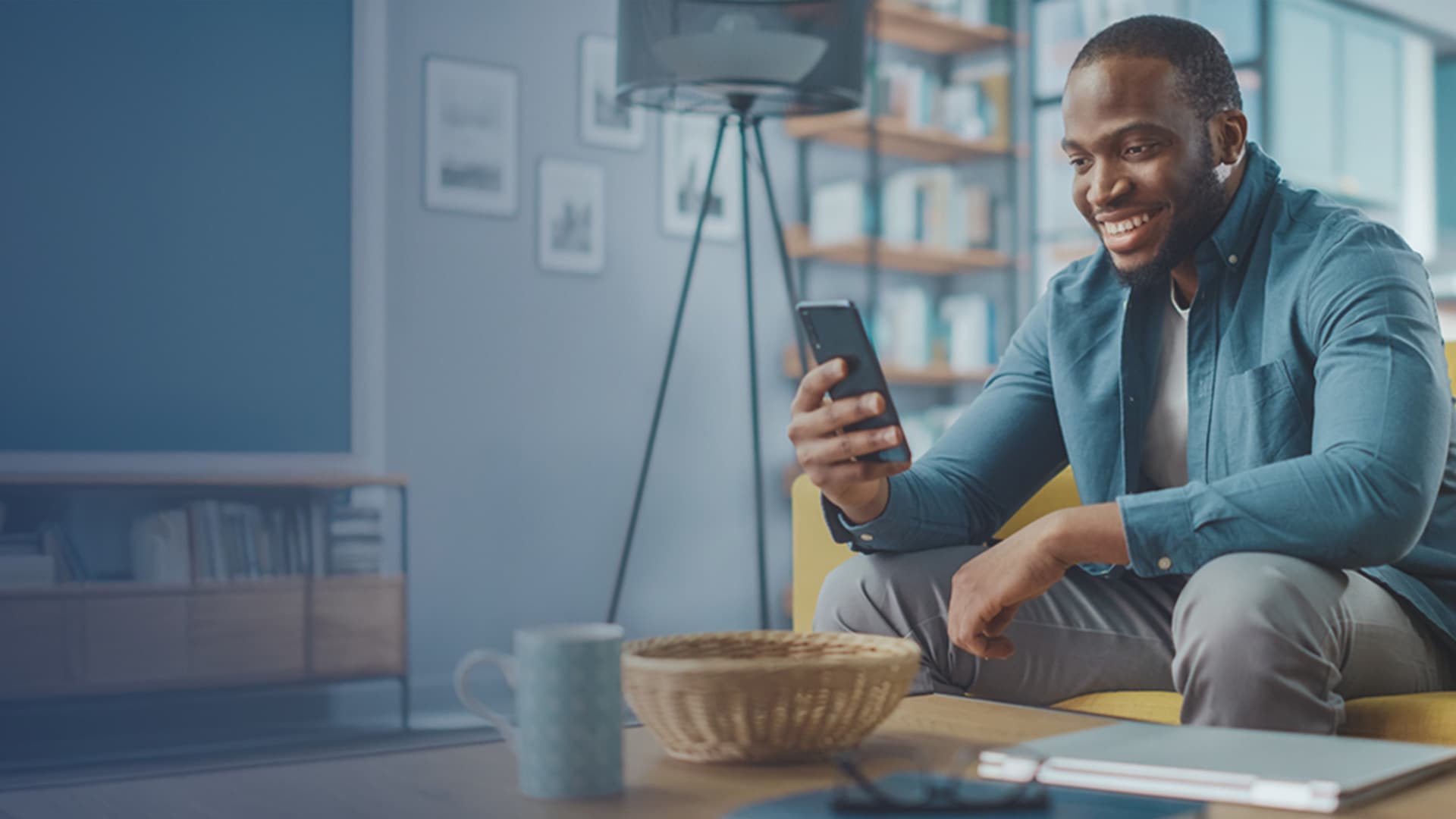 Smiling man sitting on living room couch looking at his smartphone